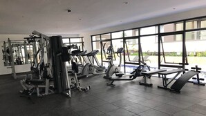 Een sportschool met diverse fitnessapparaten, grote ramen en een betegelde vloer.