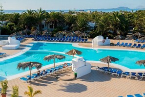 Zona de piscina amb gandules blaves, palmeres i vista al mar.