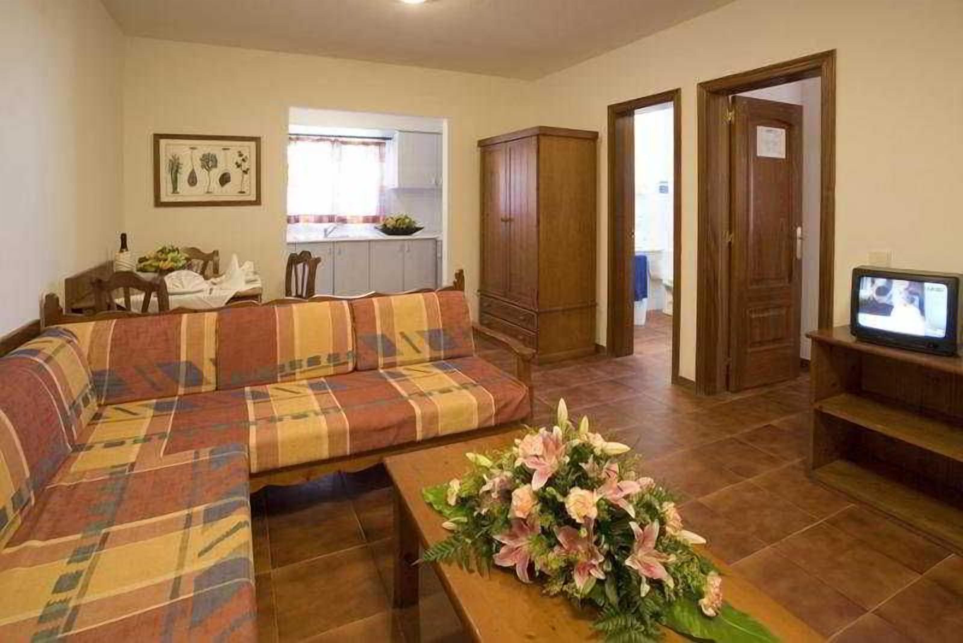 A living room with a sofa, a television, and a floral arrangement.