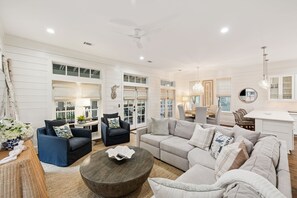 A spacious living room with a large sofa, two armchairs, a coffee table, and a dining area with a white table and chairs.