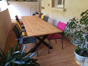 A wooden deck with a table and chairs, surrounded by potted plants.