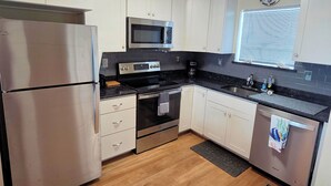 A modern kitchen with white cabinets, stainless steel appliances, a black countertop, and a wooden floor. - Tern Inn - Water Front - Townhouse, deep water dock. LINENS AND TOWELS, (Chincoteague)