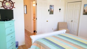 A bedroom with a bed, a dresser, a door, and a wall-mounted clock. - Tern Inn - Water Front - Townhouse, deep water dock. LINENS AND TOWELS, (Chincoteague)