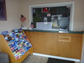 A reception desk with a wooden panel design, a glass window with a 'No Smoking' sign, and a display of various board games. - Indian Mound Motel (Fairmont City)