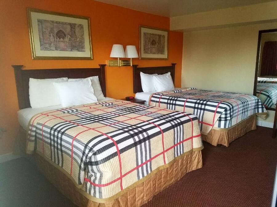 A hotel room with two beds, each with a plaid bedspread, a nightstand with a lamp, and framed pictures on the wall.
