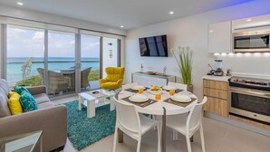 Een moderne woonkamer met een eethoek, een keuken en een grote schuifglazen deur die leidt naar een balkon met uitzicht op zee.