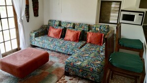 Ein Wohnzimmer mit einer Couch, zwei Hocker, einer Mikrowelle und einem Fenster mit Jalousien.