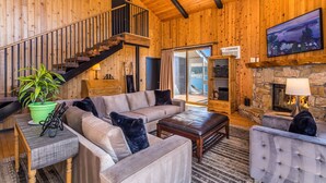 Accogliente interno di una baita in legno con una scala, un caminetto, un divano e una televisione.