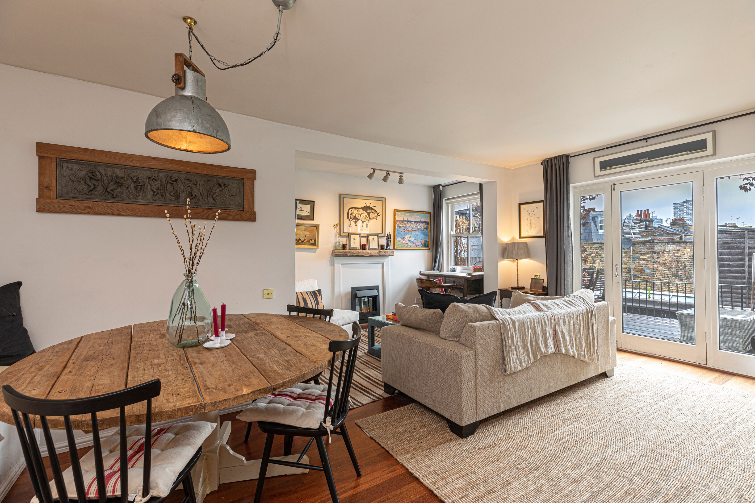 A cozy living room with a fireplace, a dining area with a wooden table, and a sofa with a view through large windows.