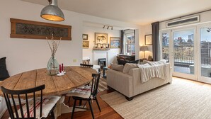A cozy living room with a fireplace, a dining area with a wooden table, and a sofa with a view through large windows. - JOIVY Stylish 2-bed Flat w/ Terrace Near Battersea Park (London)