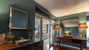 A room with a wooden dresser, a mirror, and a table with a lamp. There is a door leading to another room. - JOIVY Stylish 2-bed Flat w/ Terrace Near Battersea Park (London)