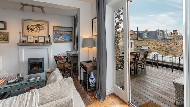 A cozy living room with a fireplace, a sofa, a dining table, and a balcony with a view of the city. - JOIVY Stylish 2-bed Flat w/ Terrace Near Battersea Park (London)