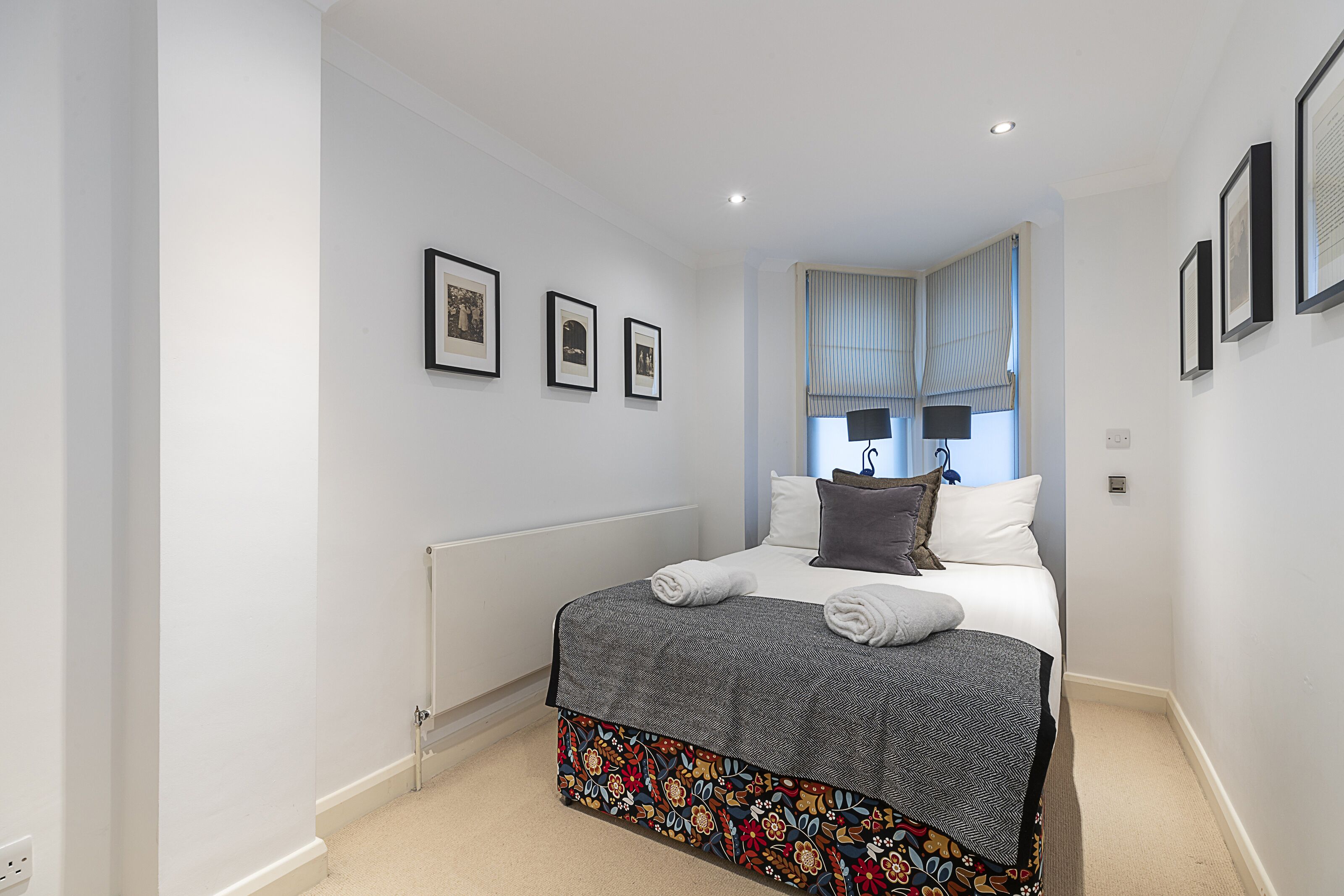 A bedroom with a bed, a radiator, and three framed pictures on the wall.