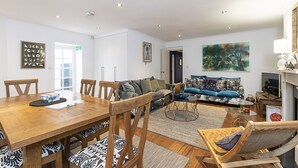 Una sala de estar moderna con una mesa de comedor de madera, asientos cómodos y un cuadro grande en la pared.