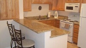 A kitchen with wooden cabinets, a granite countertop, a stove, a microwave, and two bar stools. - Desert Diamond Retreat by Mesquite Vacation Rentals: Pet Friendly with Community Amenities and $510 in free daily activities (Mesquite)