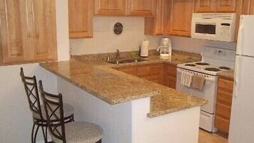 A kitchen with wooden cabinets, a granite countertop, a stove, a microwave, and two bar stools.