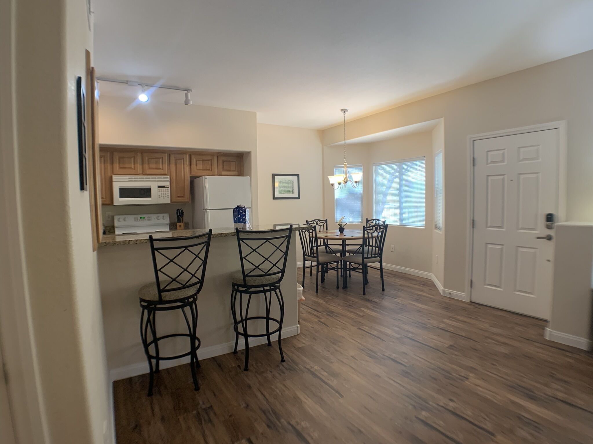A modern kitchen with wooden cabinets, a microwave, and a refrigerator. There is a dining area with a table and chairs.
