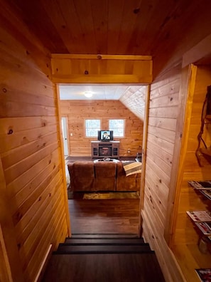 Een houten cabin-interieur met een trap naar een woonruimte, compleet met een bank, televisie en een open haard.