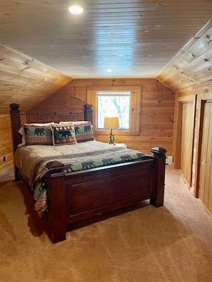 Een slaapkamer met houten lambrisering, een bed, kussens, een nachtkastje en een raam.