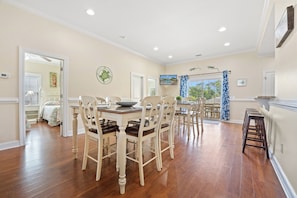 A dining area with a wooden table and chairs, a television mounted on the wall, and a view of the outdoors through a window. - Fun In The Sun, Luxury Beach House with Pool, Blocks from Beach (North Myrtle Beach)