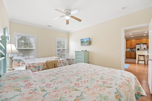 A bedroom with two beds, a ceiling fan, and a view of a kitchen through an open door. - Fun In The Sun, Luxury Beach House with Pool, Blocks from Beach (North Myrtle Beach)