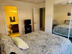 A bedroom with a large bed, a television on a stand, a bathroom with a toilet and sink, and a door leading to another room. - East Haven by Mesquite Vacation Rentals with Private Balcony with $510 in free daily activities (Mesquite)