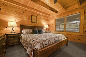 A wooden cabin bedroom with a bed, two bedside tables, lamps, and a window with blinds.
