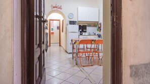 A narrow hallway leading to a kitchen with a dining table and chairs, a refrigerator, and a clock on the wall.
