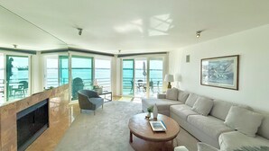 Ein großzügiger Wohnraum mit Kamin, einer Couch, einem Couchtisch und Meerblick durch große Fenster.