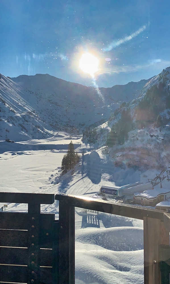 Un paisaje montañoso nevado con cielo despejado y el sol brillando intensamente.