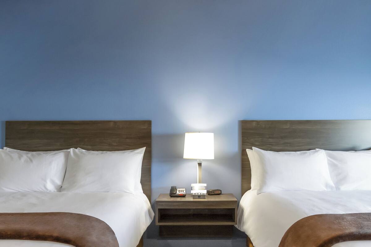 Een hotelkamer met twee bedden, een nachtkastje met een lamp en een telefoon.
