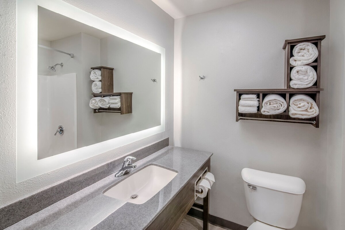 A bathroom with a large mirror, a sink, a toilet, and shelves with towels.