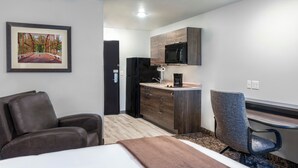 Une chambre d’hôtel équipée d’un lit, d’un bureau, d’une chaise, d’une kitchenette et d’un tableau encadré au mur.