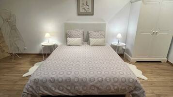A bedroom with a large bed, two bedside tables with lamps, a wardrobe, and an air conditioning unit on the wall.
