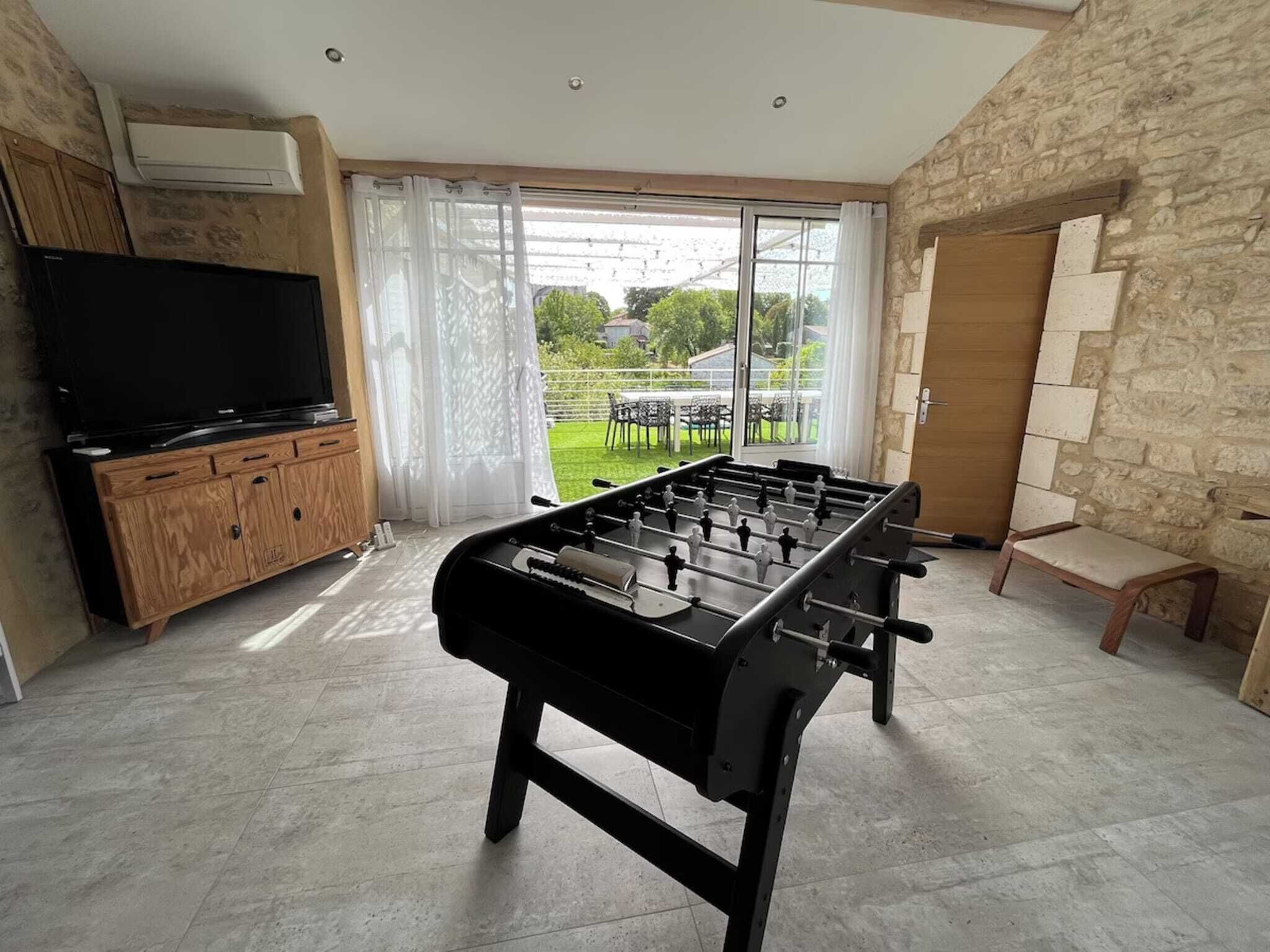 A room with a foosball table, a television on a wooden cabinet, and a stone wall.