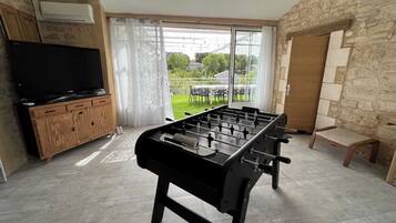 A room with a foosball table, a television on a wooden cabinet, and a stone wall.