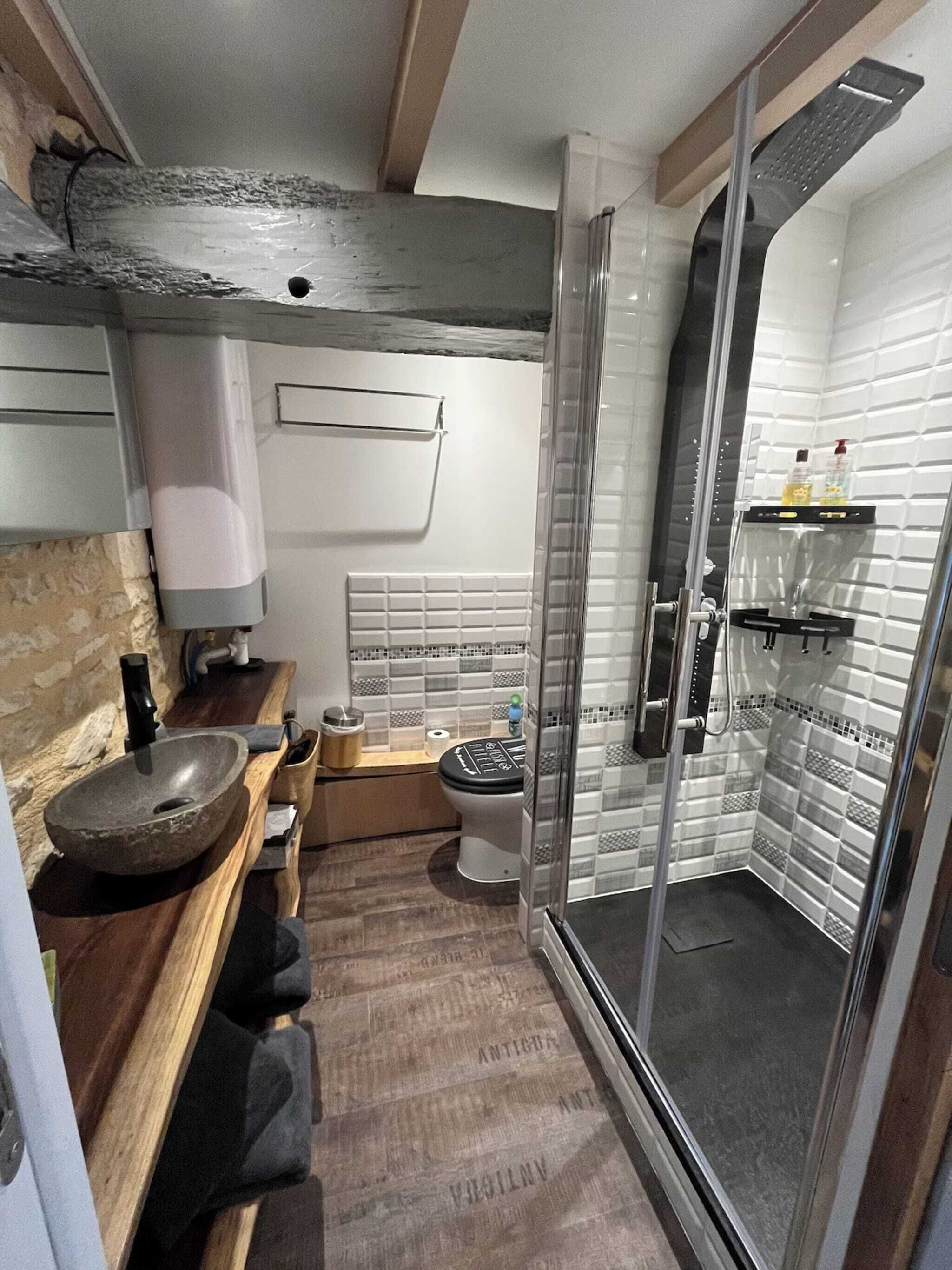 Een moderne badkamer met een stenen wastafel, een houten aanrechtblad, toilet en een douchecabine met glazen wanden.