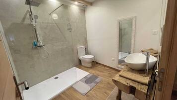 Een moderne badkamer met een douchecabine van glas, een toilet, een wastafel met houten blad en een grote spiegel.
