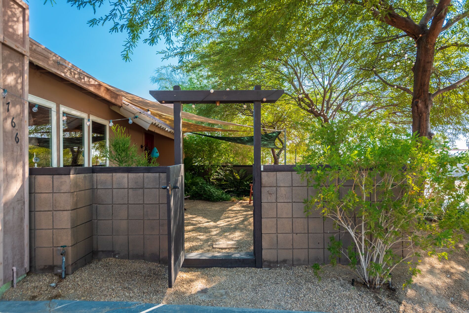 Una entrada protegida con un pérgola, un sendero de grava y un edificio de fachada con tejas.