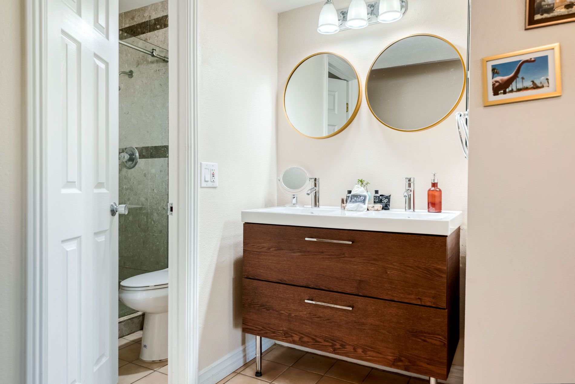 Une salle de bain avec des toilettes blanches, une douche avec une porte en verre, un meuble-lavabo avec un miroir et un évier.