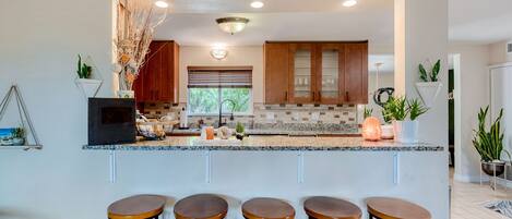 A modern kitchen with wooden cabinets, a granite countertop, and bar stools.