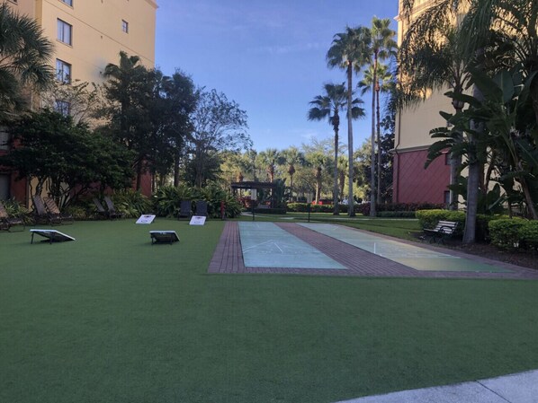 A courtyard with artificial grass, a shuffleboard court, and palm trees. - 2BR-Dlx Inside Disney Gates-5 Pools, 2 Lazy Rivers, SPLASH pad, Mini Golf & More (Lake Buena Vista)