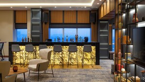 A modern bar area with a view of the cityscape, bar stools, a seating area with a sofa, and a bookshelf with decorative items. - Courtyard by Marriott Tashkent (Tashkent)
