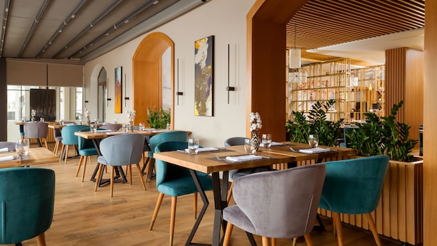 A modern restaurant interior with wooden tables, teal and gray chairs, and large windows. - Courtyard by Marriott Tashkent (Tashkent)