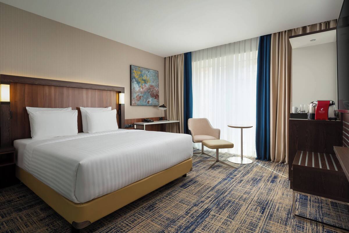 A hotel room with a large bed, a desk, a chair, a small table, and a mirror.
