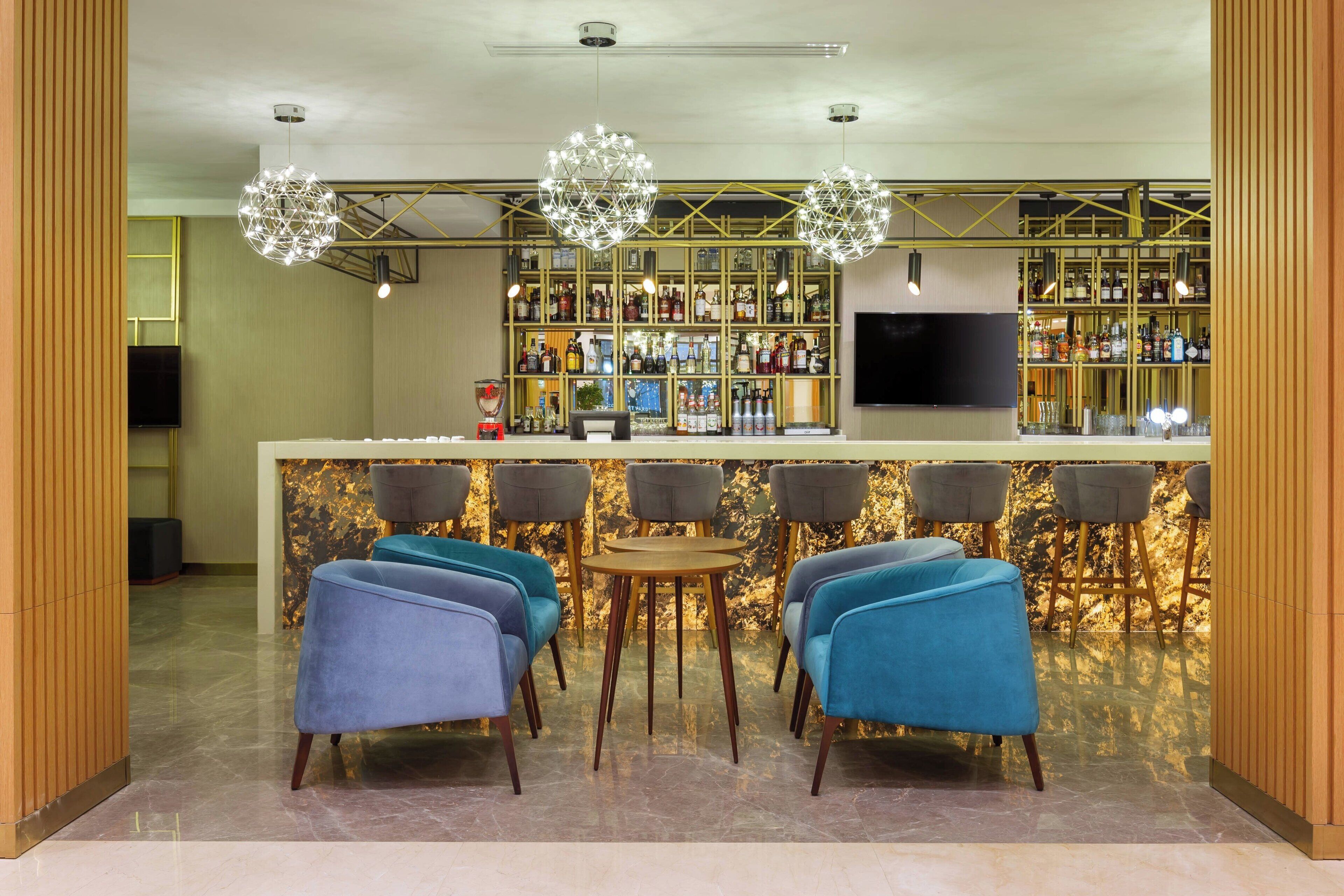 A bar area with a marble countertop, bar stools, and a television screen.
