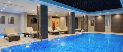 Una piscina interior con sillones de descanso y techo de azulejos.