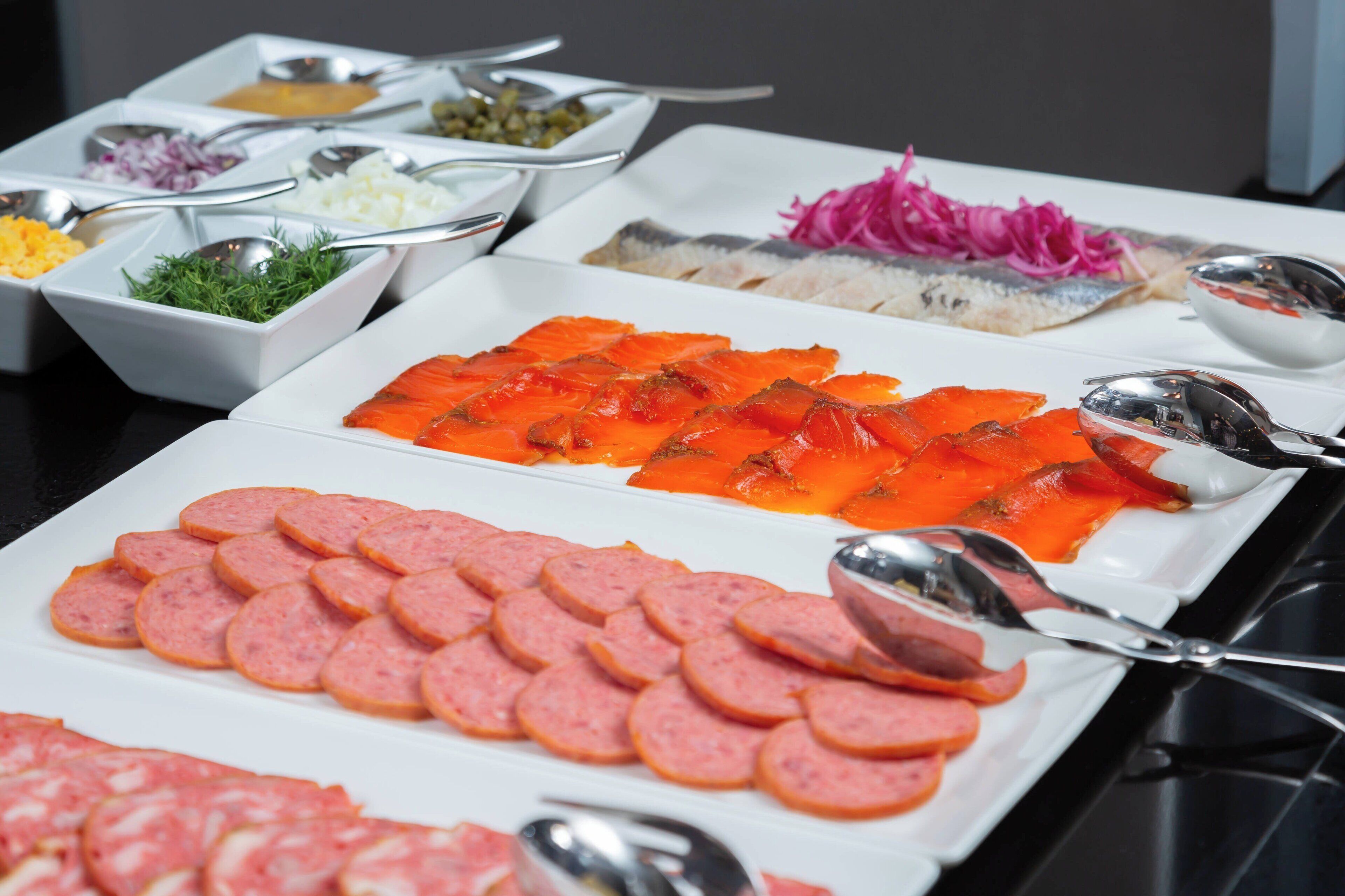 A buffet with various food items including sliced salmon, sausage, and pickled vegetables.