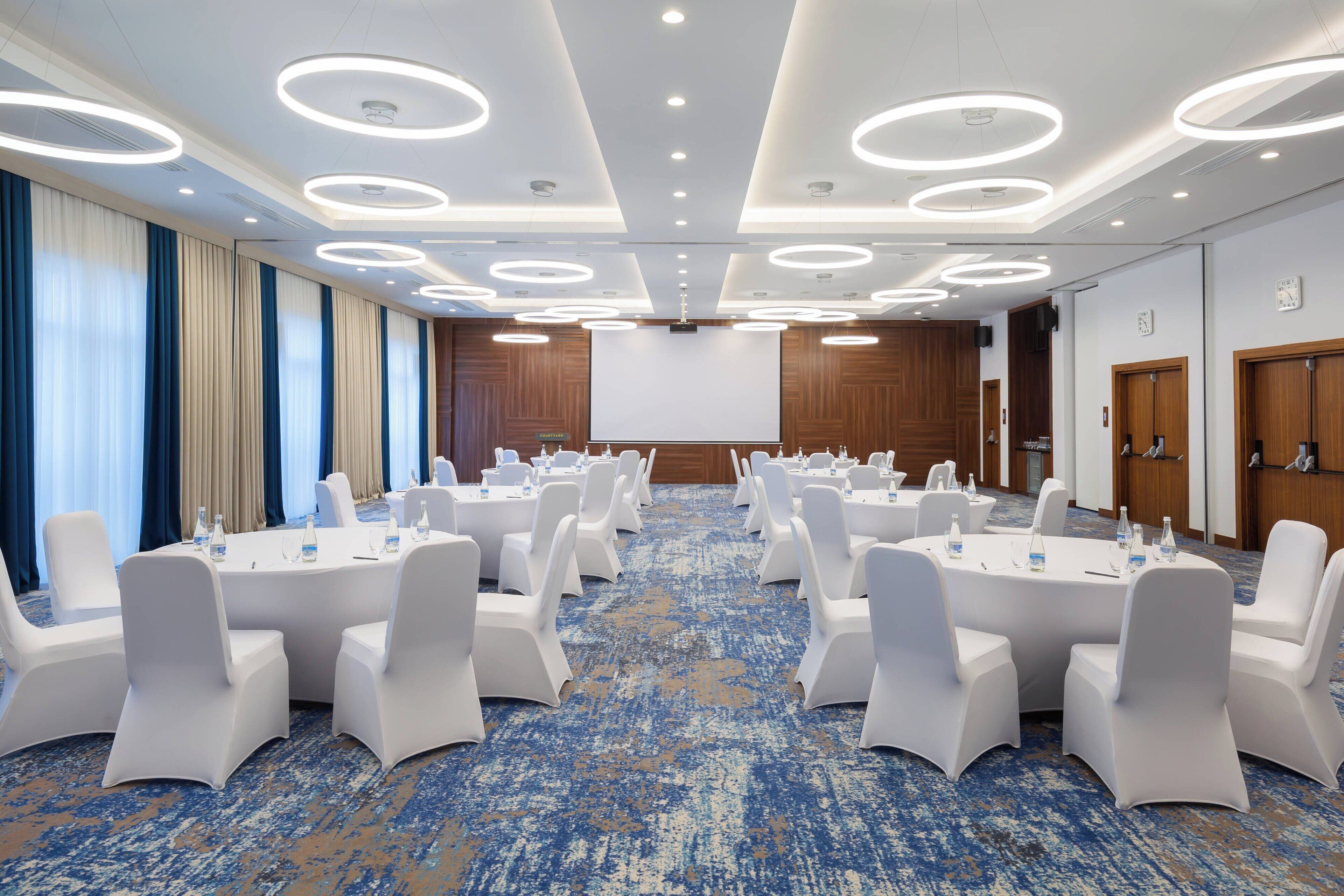 A conference room with round tables, white chairs, and a blue carpet.