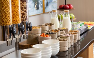 Un bufé con diversos alimentos, entre ellos cereales, nueces, frutas secas y leche.